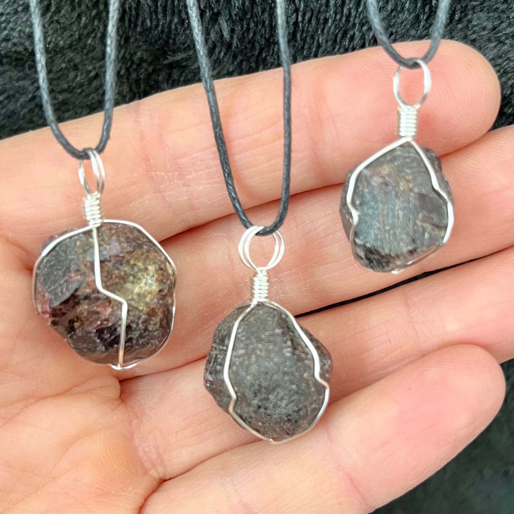 3 silver wire wrapped garnet crystal pendants attatched to adjistable black cords.  pendant vary in diameter from 1/2" to 3/4"