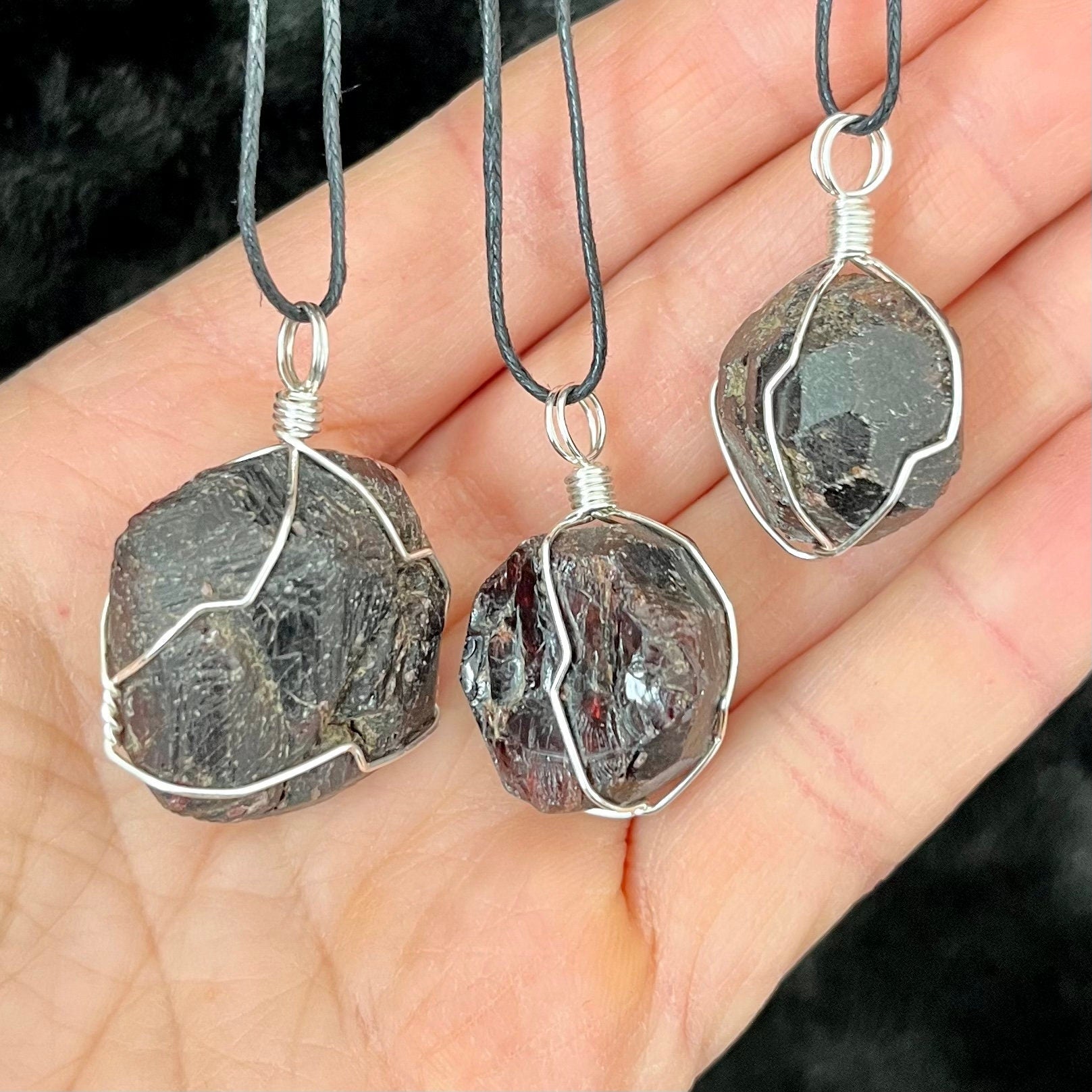 3 silver wire wrapped garnet crystal pendants attatched to adjistable black cords.  pendant vary in diameter from 1/2" to 3/4"