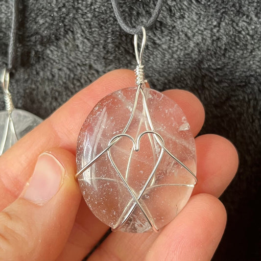 clear quartz worry stone beautifull silver wire wrapped to create a heart shape in the center.  pendant is attatched to an adjistable black cord and is approximately 1 3/4" long.