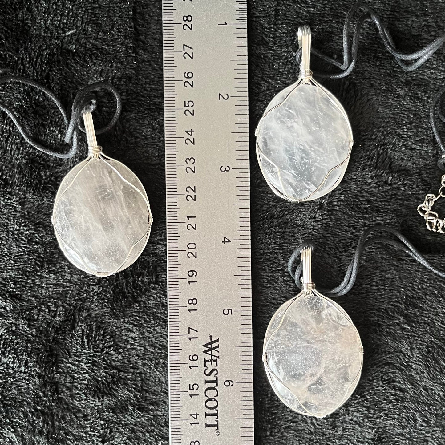 3 clear quartz worry stones beautifully silver wire wrapped in a way that frames the stone beautifully allowing access to the smoothe concave side on the back.  pe dants are approximately 2 inches long and attatched to adjustable black cords, and displayed next to a ruler