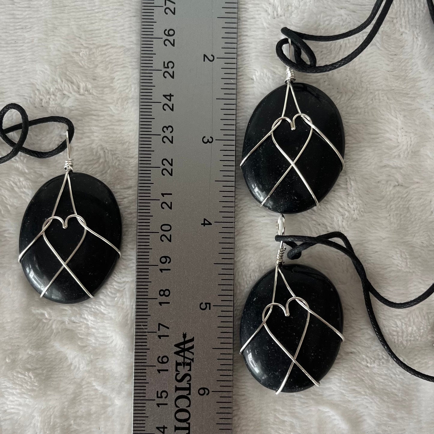 Silver wire wrapped obsidian worry stone pendants, with adjustable black cords.  obsidian crystal are approximately 1 1/2" long.  wire males a heart shape in the middle of the stones.  Necklaces are displayed next to a ruler