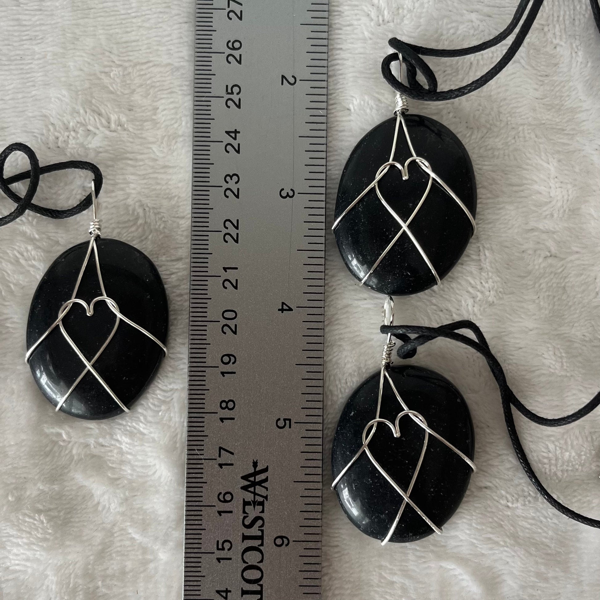 Silver wire wrapped obsidian worry stone pendants, with adjustable black cords.  obsidian crystal are approximately 1 1/2" long.  wire males a heart shape in the middle of the stones.  Necklaces are displayed next to a ruler