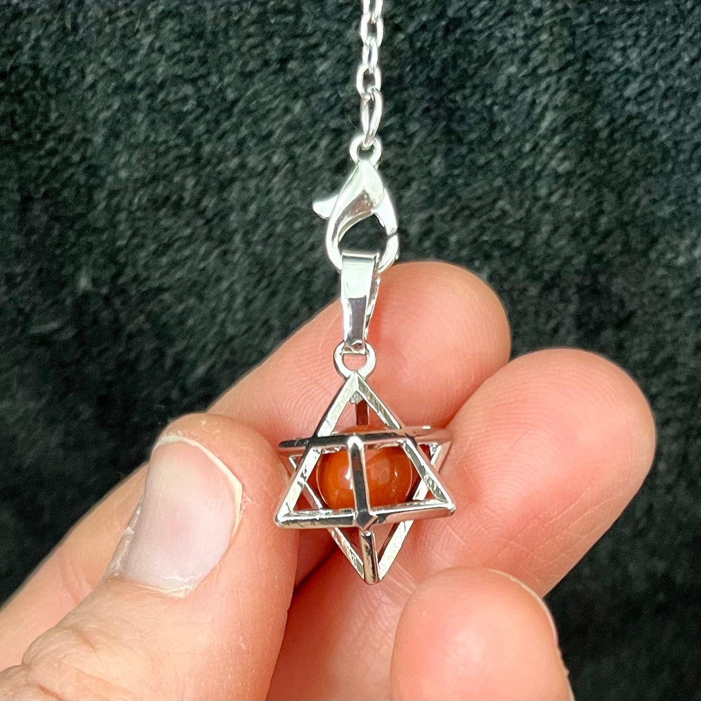 "Close-up of a red Jasper sphere encased within a silver Merkaba pendulum.